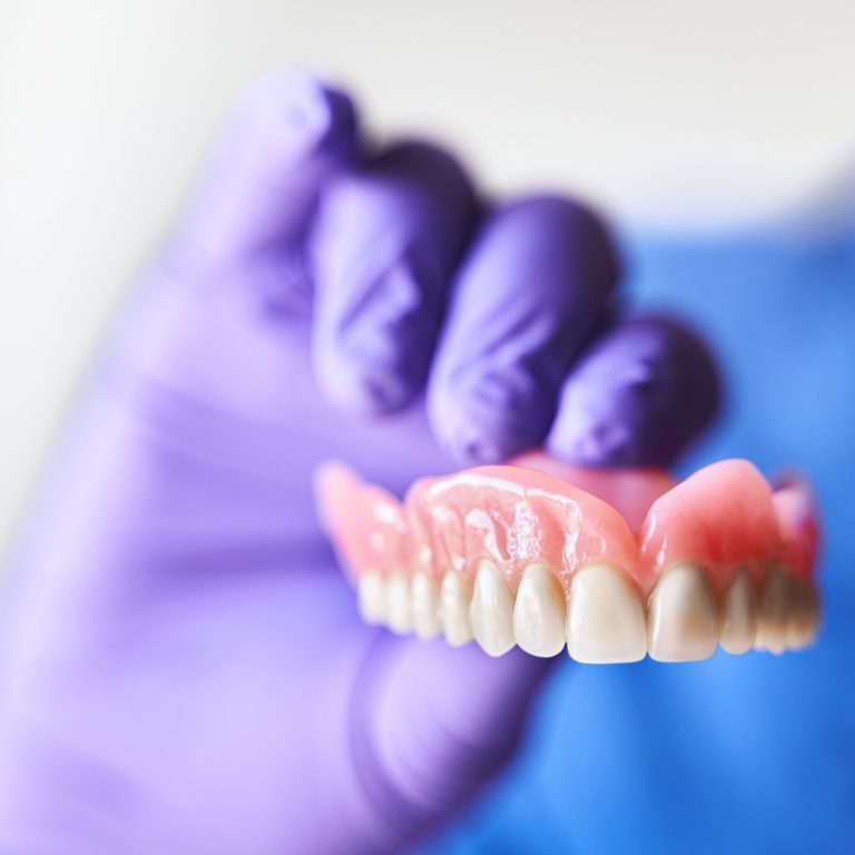 Dentist,With,Purple,Gloves,Holding,Dentures,In,Hand.,Concept,Of